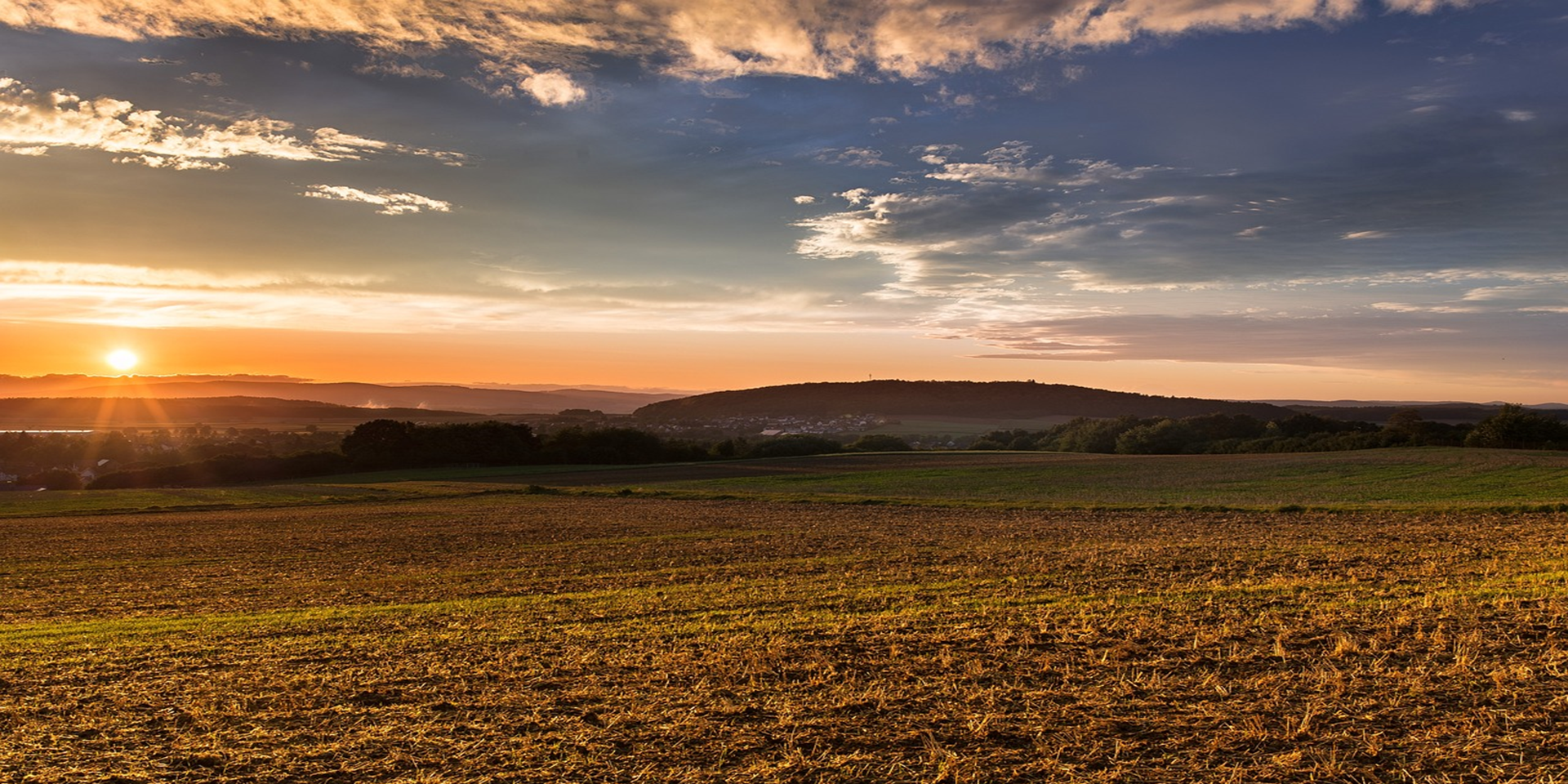 Un vaste champ avec un coucher de soleil et des montagnes au loin